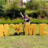 Raeanne Beckner stands in front of a huge Home sign with the flying WV